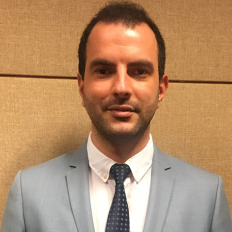 A man in a suit posing in front of a beige background.
