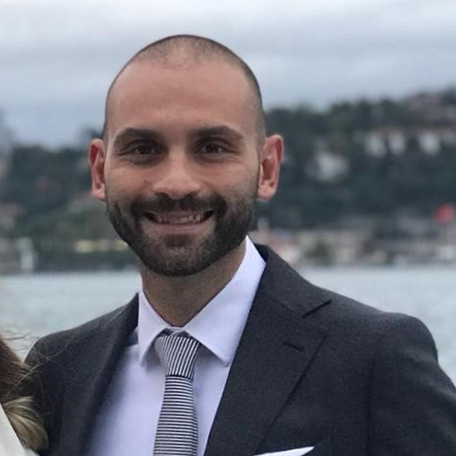 Bir adam deniz kenarında gülümseyerek poz veriyor.