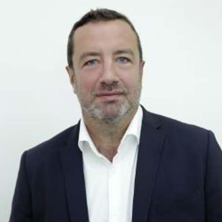 Man in a dark suit and white shirt standing against a white background.