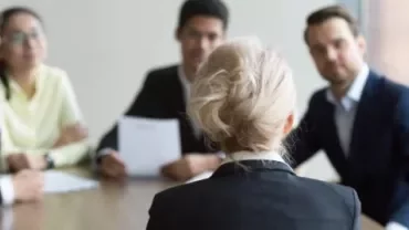 Woman facing four people in a business meeting.