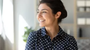 Woman in polka dot shirt smiling indoors.