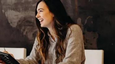 A woman smiling while holding a notepad.
