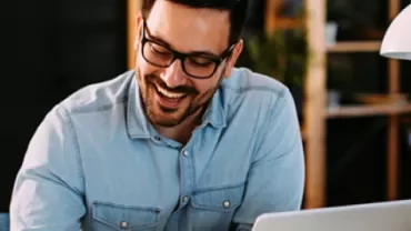 Man smiling while working on a laptop in an office.