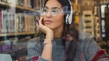 Woman in headphones sits by a bookshelf, looking thoughtful.