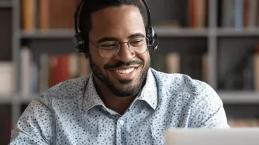 Man wearing glasses and headphones, working on a laptop.