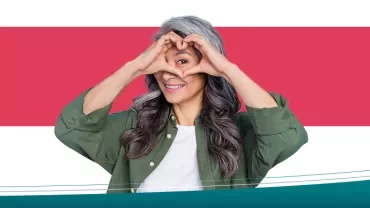 Kadın kalp şekli yapan ellerle kamera karşısında gülümsüyor.