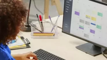 A person scheduling events on a calendar displayed on a monitor.