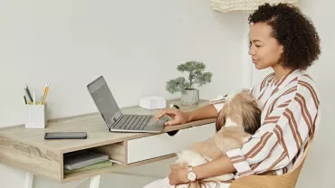 Woman working on a laptop at home with her dog in her lap.