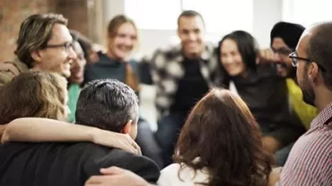 Bir grup insan kol kola durmuş, mutlu görünüyor.