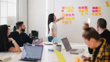 Person pointing at sticky notes on a whiteboard during a meeting.