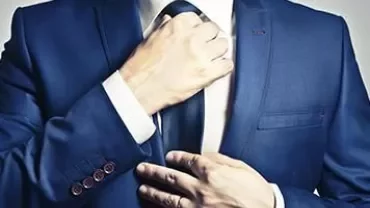 Man adjusting a tie while wearing a blue suit.
