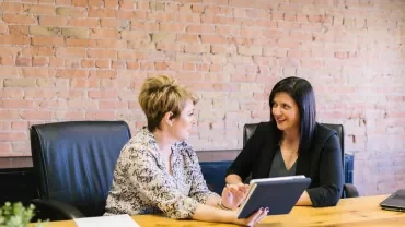 Two women discussing something while looking at a tablet.