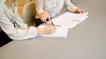 İki kişi masa üzerinde belgeleri inceliyor.
