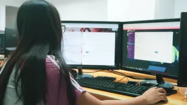 Bilgisayar ekranlarına bakan bir kadın, masasında çalışıyor.