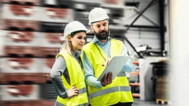 Two construction workers wearing safety gear reviewing a tablet.