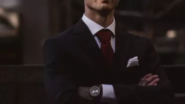 Man in a dark suit and red tie with arms crossed.