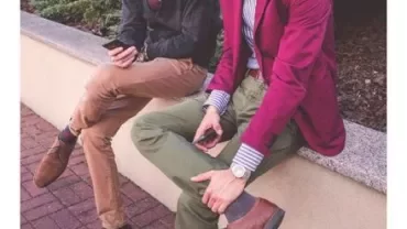 Two people sitting on a wall looking at their phones.