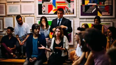 A group of people engaged in discussion in front of modern art on the wall.