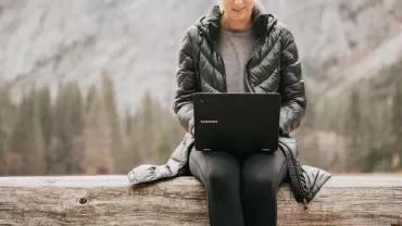 Person using a laptop while sitting on a log in nature.