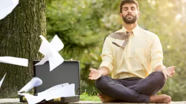 Man meditating under a tree with flying papers around him.