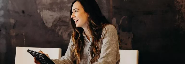 A woman smiling while holding a notepad.