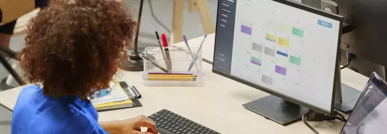 A person scheduling events on a calendar displayed on a monitor.