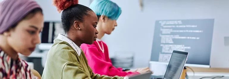 Three people working on laptops in an office setting.