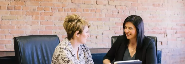 Two women discussing something while looking at a tablet.