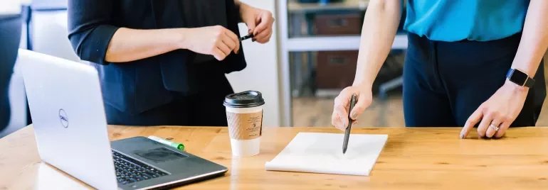 Toplantı masasında dizüstü bilgisayar ve not alan iki kişi.
