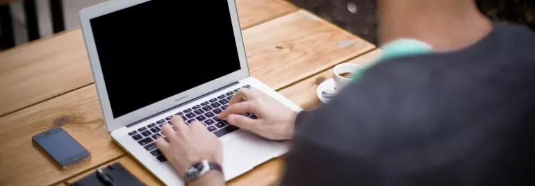 Person using a laptop on a wooden table.