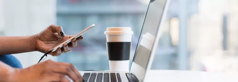 Bir kişi laptopta çalışırken cep telefonu tutuyor.