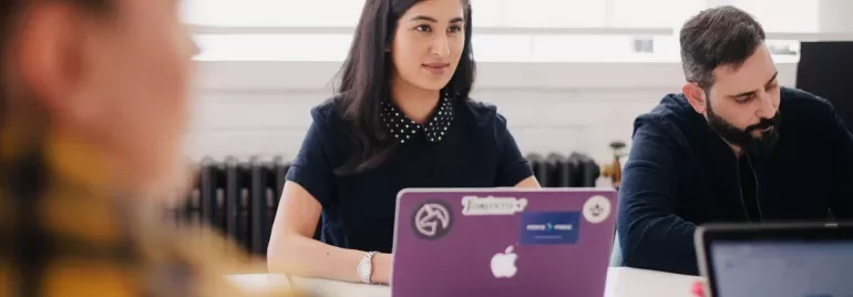 Bir kadın dizüstü bilgisayarla toplantıda oturuyor.