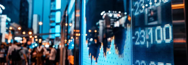 Gece şehirde bir borsa ekranı ve bulanık sokak manzarası.