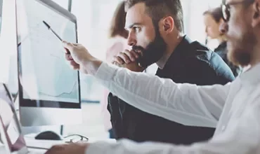 Two men working at computers, one pointing at the screen.