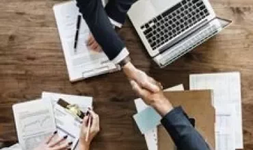 People shaking hands over a laptop in a business meeting.