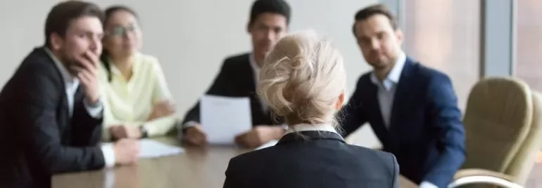 Toplantı masasında oturan bir kadın ve onu dinleyen dört kişi.