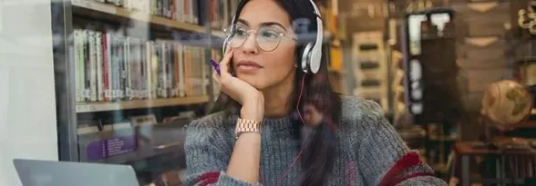 Kulaklık takan kadın kitaplık önünde düşünüyor.