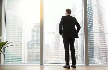 A man in a suit looking out at a cityscape through a large window.