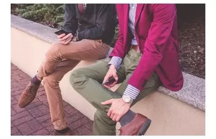 Two people sitting on a wall looking at their phones.