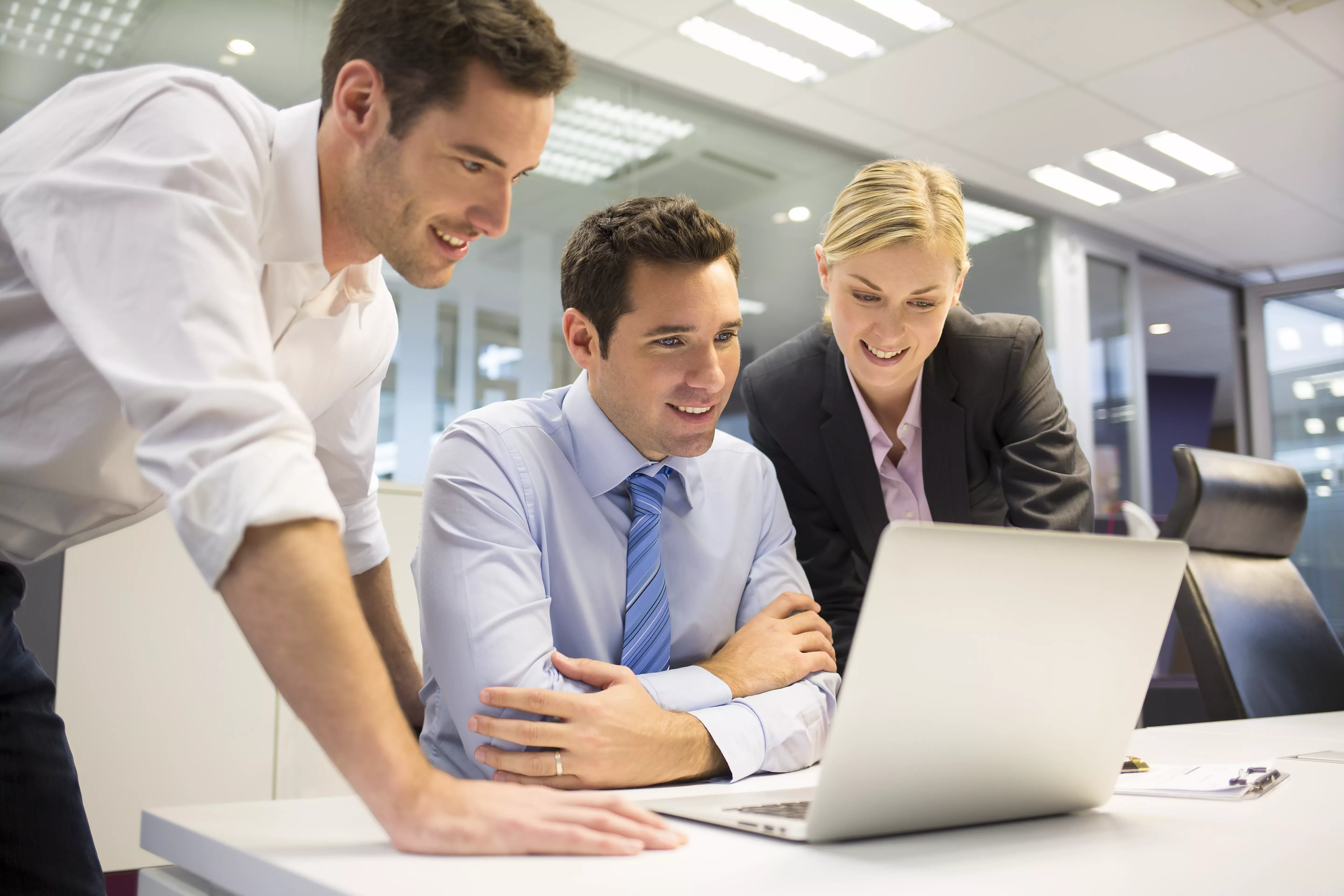 Three people looking at a laptop in an office.